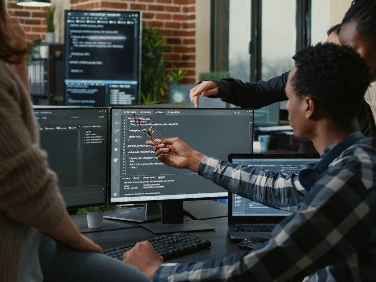 Foto Büroumgebung Person zeigt auf einen Computerbildschirm mit Programmiercode in einer Büroumgebung.